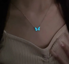Blue luminous butterfly pendant necklace on a silver chain, worn near the collarbone with a glowing butterfly charm.